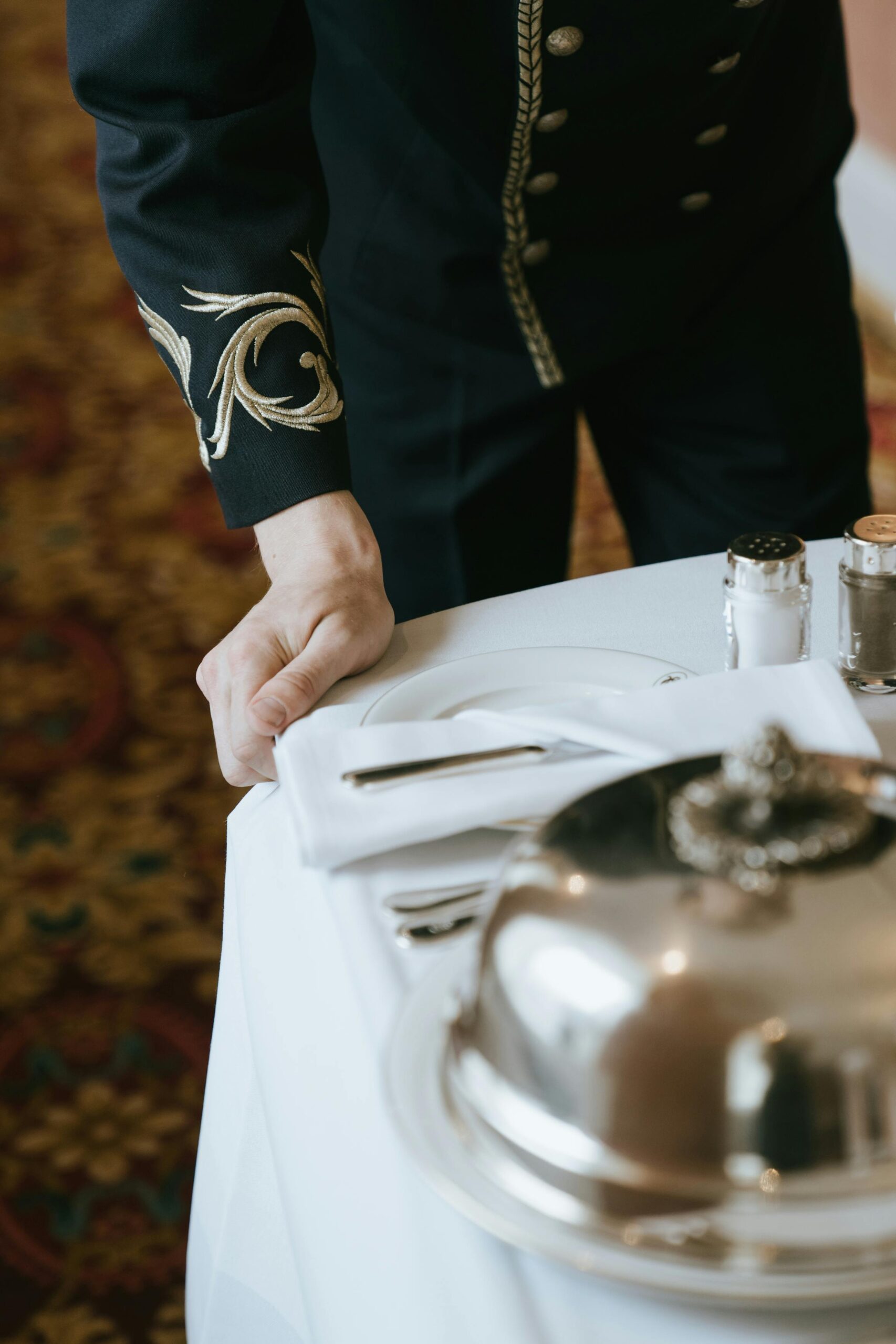 A hotel staff member in uniform setting up a luxurious room service tray.
